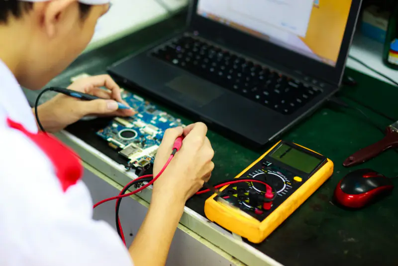 Teknisyen laptop anakartını ölçü aletiyle test ediyor
